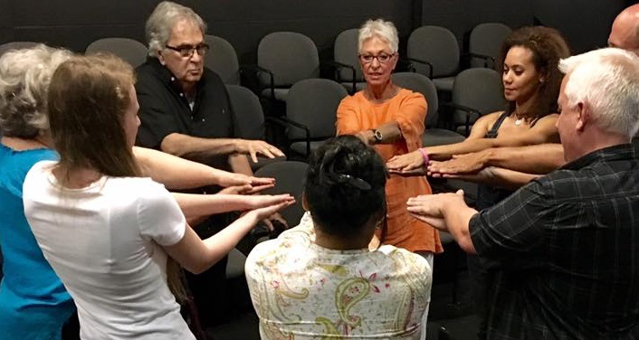 image of Improv Basics Class " Mirror", men and women standing in a circle with arms held forward
