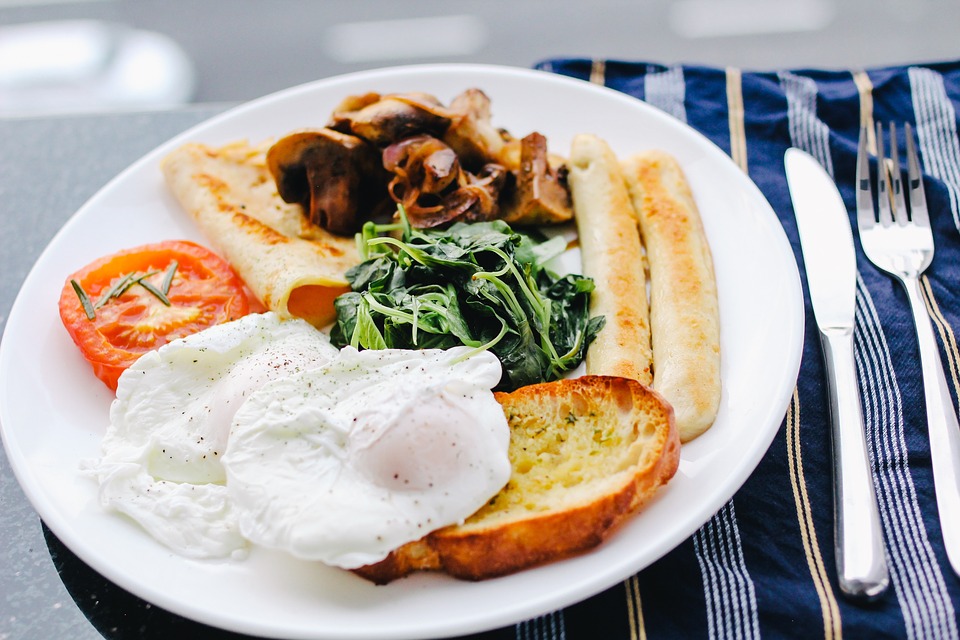 Image contains eggs, spinach, bacon, tomatoes, toast, and sausage on a plate.