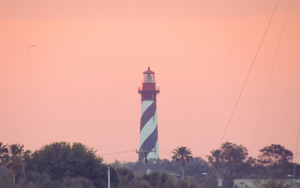 The of St. Augustine Lighthouse peaking over tree line.