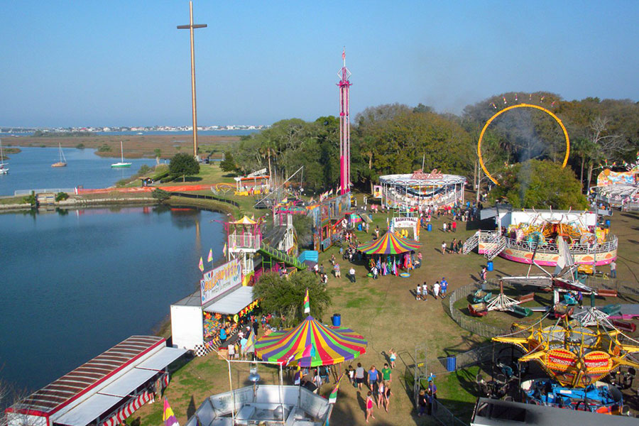 Cathedral Festival An aerial view of a large park that has theme park rides, people walk, and a giant cross.
