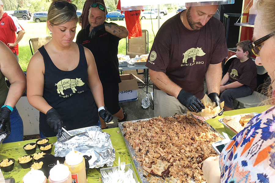 Two people serving pulled pork and macaroni and cheese to another person.