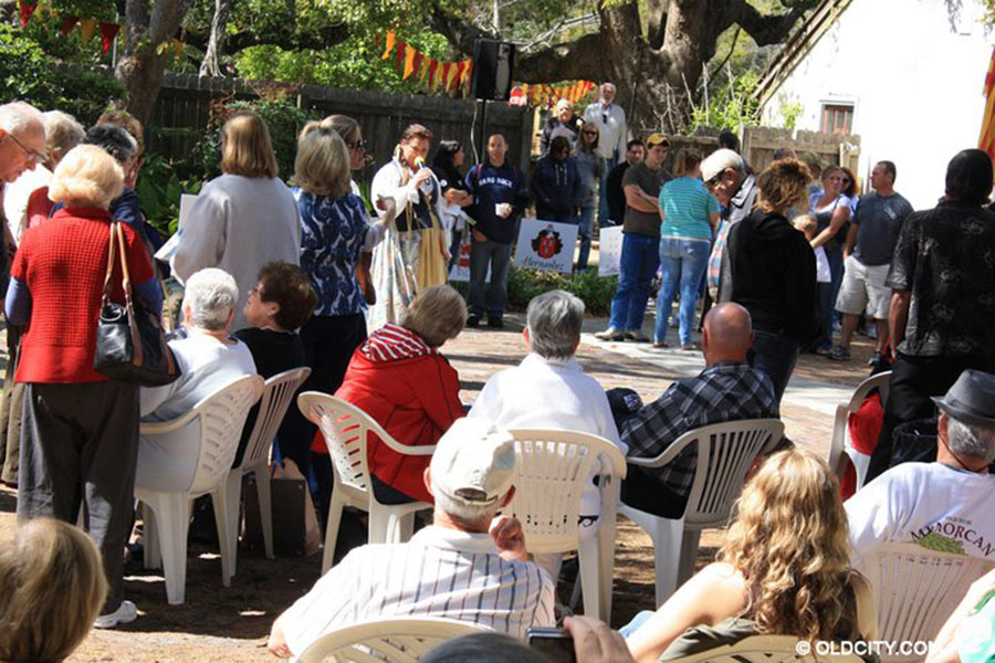 A crowd of people sitting, standing around two other people with a microphone at Menorcan Heritage Celebration