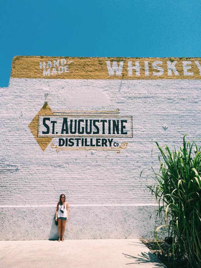 This image contains a woman standing in front of the St. Augustine Distillery.