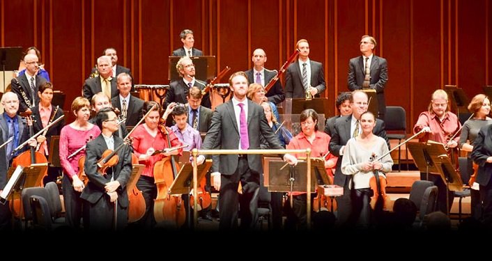 photo of Jacksonville Symphony Orchestra; men and women on stage playing various instruments