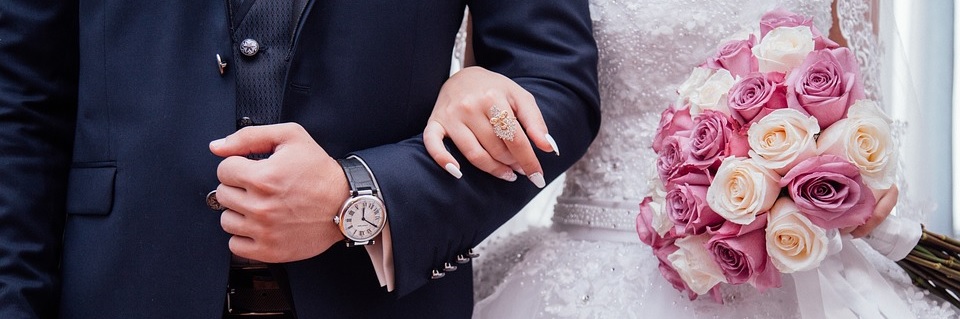 Image contains a close up of a bride and groom locking arms, with flowers in brides hand.