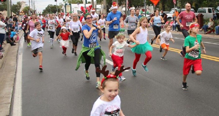 image of runners, young and old, from young boys and girls to adults running in annual Reindeer Run. Some wearing reindeer antlers, some red and green for Chistmas season