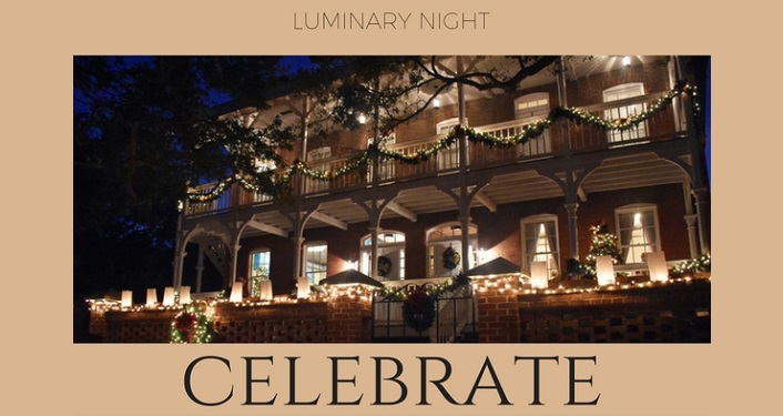 image of the front of the Lighthouse at nighttime with garland decorating the railing and several luminaries lit up for Luminary Night at the Lighthouse
