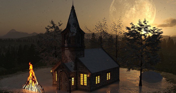 image of church at dusk with sun setting in background, lit Christmas tree in front of church