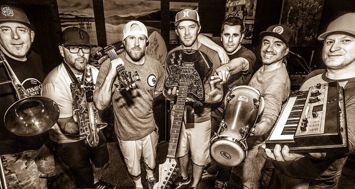 Reggae-rock favorites Slightly Stoopid press photo; black & white image of 7 men standing in semi-circle each one holding a different instrument; bongo drums, guitar, keyboard, trumpet, sax.