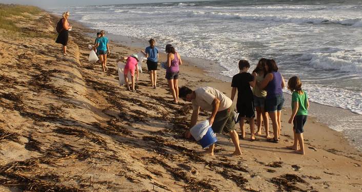 image of young adults, male & female, and couple of women all wearing shorts, picking up debris on beach during GTM Beach Cleanup