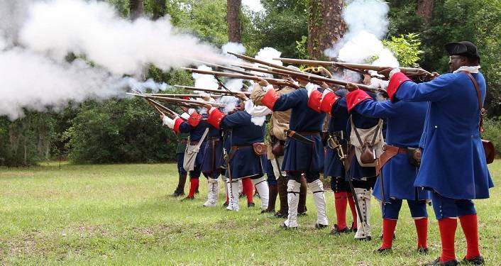 men dressed in 18th century clothing firing muskets during Militia Muster at Fort Mose
